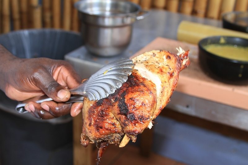 Hand holding a grilled jerk chicken quarter fresh off the grill